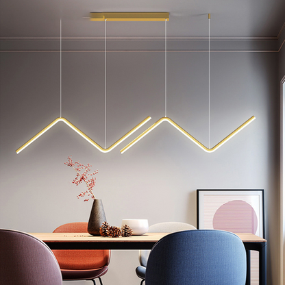 Lustre pendente moderno em formato tubular dourado em sala com mesa de madeira e cadeiras coloridas