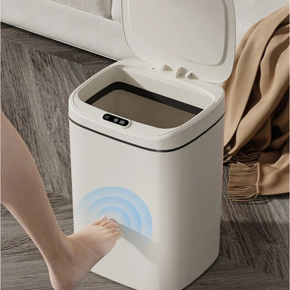 Lixeira automática branca com tampa aberta, ativada por sensor de pé em piso de madeira com manta marrom ao lado