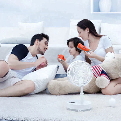 Família alegre sentada no chão da sala com ventilador portátil e comendo melancia