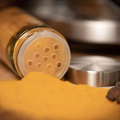 Frasco de vidro aberto com tempero amarelo em pó e tampa metálica ao lado