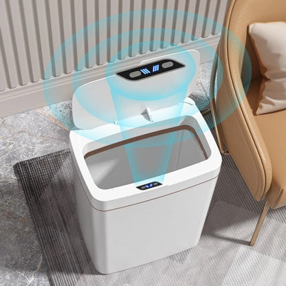 Lixeira automática branca aberta com sensor de movimento, localizada ao lado de poltrona bege em ambiente interno