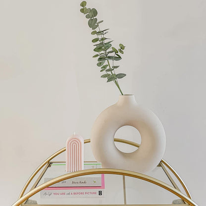 Vaso decorativo branco redondo com planta verde, vela rosa arco-íris e livros em mesa dourada