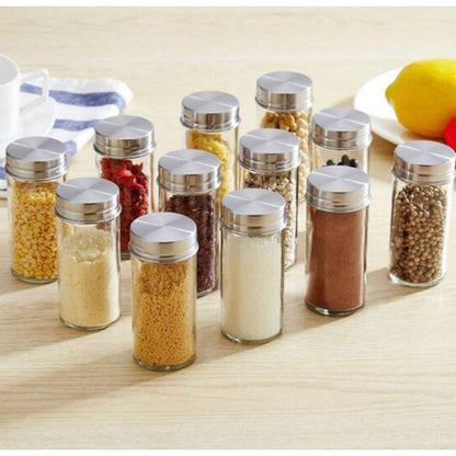 Frascos transparentes com tampas metálicas contendo especiarias e grãos variados sobre mesa de madeira