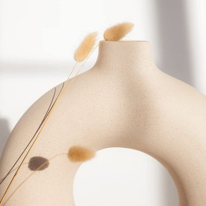 Vaso decorativo bege fosco em formato circular com duas hastes secas em fundo claro