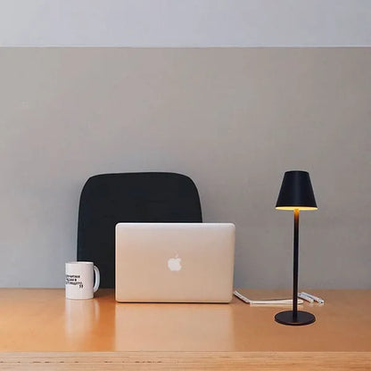 Mesa de escritório minimalista com laptop Apple, caneca branca, caderno, canetas e luminária preta sobre fundo cinza