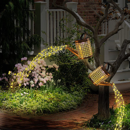 Luminárias decorativas em formato de regadores com luzes LED simulando água iluminando jardim à noite