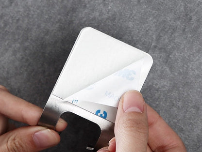 Mãos retirando o papel protetor adesivo de um suporte metálico quadrado para parede