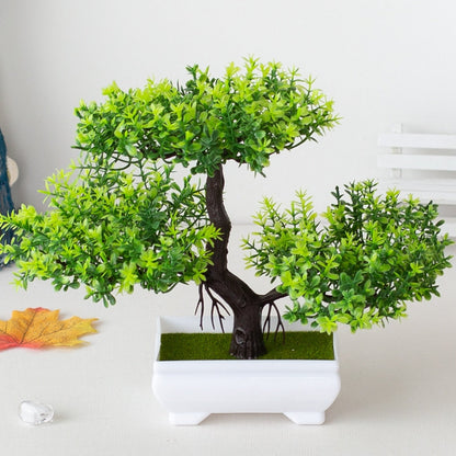 Bonsai artificial verde em vaso branco sobre mesa clara com folha de outono ao lado