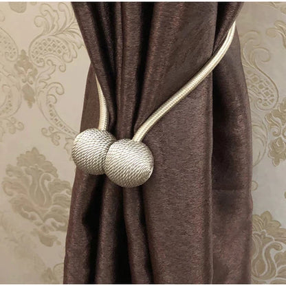 Cortina marrom presa com prendedor de corda branca com bolas decorativas em ambiente com parede com papel de parede clássico