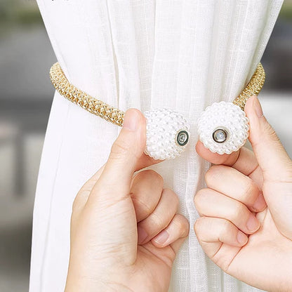 Mãos segurando presilha magnética dourada com pérolas para cortina branca