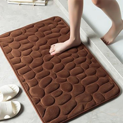 Tapete de banho castanho com textura de pedras e pés descalços em piso de banheiro