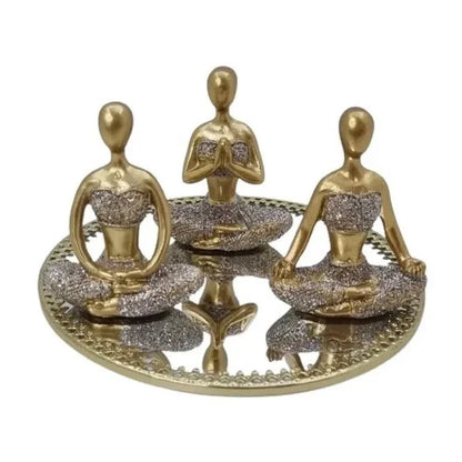 Esculturas douradas de figuras femininas meditativas com detalhes brilhantes sentadas em bandeja decorativa