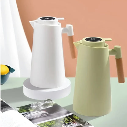 Garrafa térmica com termômetro digital no topo, uma branca e outra bege com alça de madeira, sobre mesa