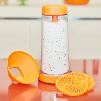 Purificador de ambiente com tampa e filtro laranja, com infusão branca e partículas visíveis, sobre mesa vermelha