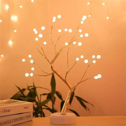 Luminária decorativa em formato de árvore LED com luzes brancas, sobre mesa com livros e planta ao fundo