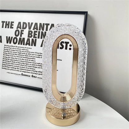 Luminária decorativa oval cristal com base dourada, em mesa branca, com quadro de texto ao fundo