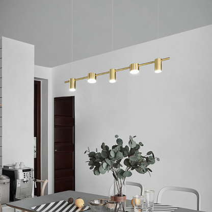 Lustre pendente dourado moderno com quatro focos iluminando mesa de jantar com planta e copos