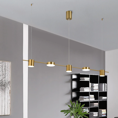 Luminária pendente dourada moderna iluminando estante preta com livros em sala com parede cinza