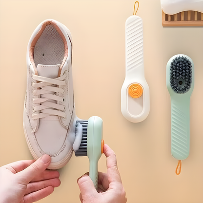 Mão limpando tênis branco com escova elétrica ao lado de escovas adicionais em fundo bege