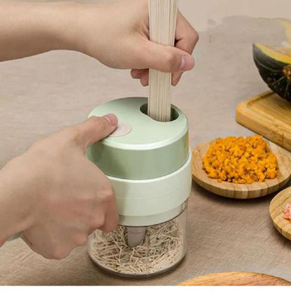 Mãos usando moedor manual de alimentos para processar raízes secas, com ingredientes em pratos de madeira ao fundo