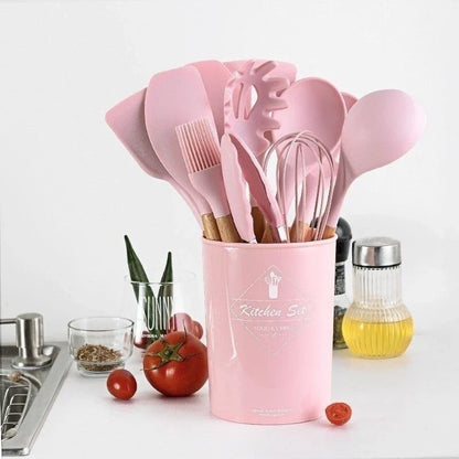 Conjunto de utensílios de cozinha rosa em suporte, com tomate, azeite e tempero na bancada