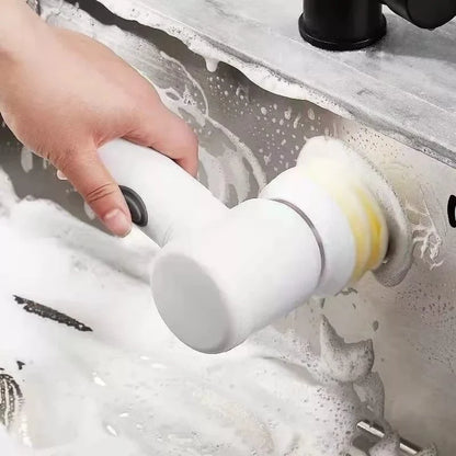 Mão segurando escova elétrica branca limpando pia de aço inox com espuma de sabão