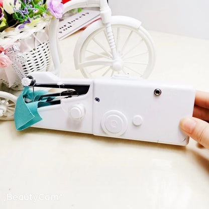 Máquina de costura portátil branca operada com uma mão, tecido azul e decoração com flores e bicicleta branca ao fundo